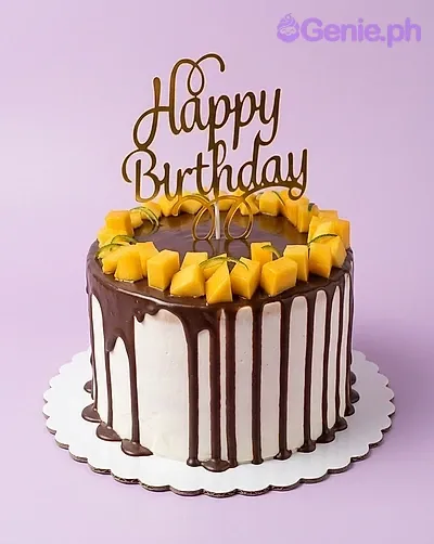 A white 1 Tier cake, Mango Chocolate themed, with a gold Happy Birthday topper, mango cubes, and green leaves. A white 1 Tier cake, Mango Chocolate themed, with a gold Happy Birthday topper, mango cubes, and green leaves.