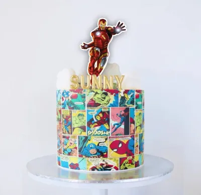 Marvel Avengers comic book themed cake with a large Iron Man printout topper and gold Sunny name topper on white icing clouds. Marvel Avengers comic book themed cake with a large Iron Man printout topper and gold Sunny name topper on white icing clouds.