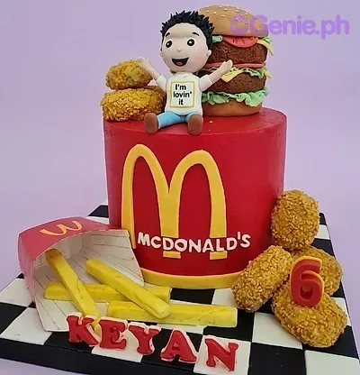 A red 1-tier fondant cake themed around McDonald's, featuring a boy figurine, burger, fries, nuggets, and M logo. A red 1-tier fondant cake themed around McDonald's, featuring a boy figurine, burger, fries, nuggets, and M logo.