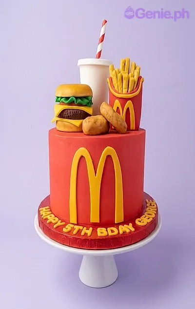 A red and yellow 1 Tier Fondant cake themed around McDonald's, featuring a fondant burger, fries, soda cup, nuggets, and a yellow 'M' logo. A red and yellow 1 Tier Fondant cake themed around McDonald's, featuring a fondant burger, fries, soda cup, nuggets, and a yellow 'M' logo.