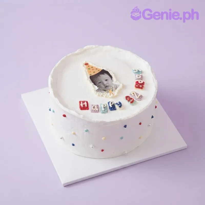 White 1 tier cake with smooth soft icing, an edible photo topper of a baby in a party hat, and scattered multicolor sugar pearls White 1 tier cake with smooth soft icing, an edible photo topper of a baby in a party hat, and scattered multicolor sugar pearls