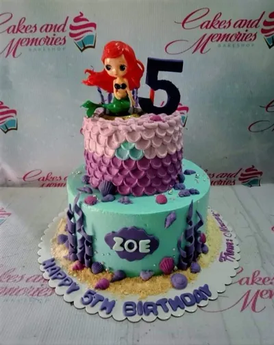 A teal and light purple two-tier Mermaid Ariel cake, with an Ariel figurine, a number 5 topper, and edible shells. A teal and light purple two-tier Mermaid Ariel cake, with an Ariel figurine, a number 5 topper, and edible shells.