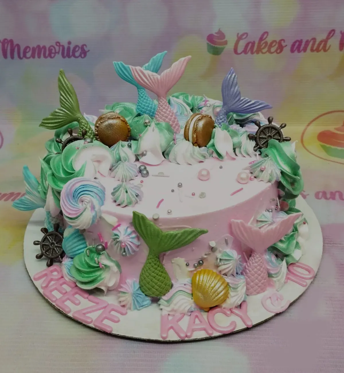 A pink and colorful 1 Tier cake themed around Mermaid, featuring mermaid tails, gold macarons, ship wheels, and edible pearls. A pink and colorful 1 Tier cake themed around Mermaid, featuring mermaid tails, gold macarons, ship wheels, and edible pearls.