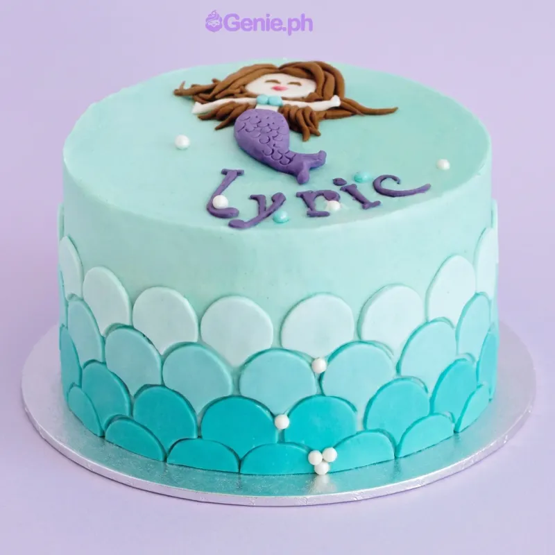 Light blue 1-tier cake with soft icing, a flat fondant mermaid topper, and ombre teal fondant scales Light blue 1-tier cake with soft icing, a flat fondant mermaid topper, and ombre teal fondant scales