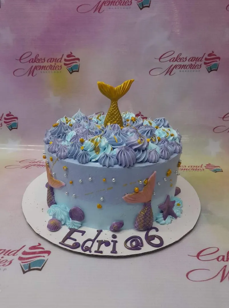 A light blue 1-tier cake themed around Mermaid, featuring a gold mermaid tail, purple and teal icing, and edible sea elements. A light blue 1-tier cake themed around Mermaid, featuring a gold mermaid tail, purple and teal icing, and edible sea elements.