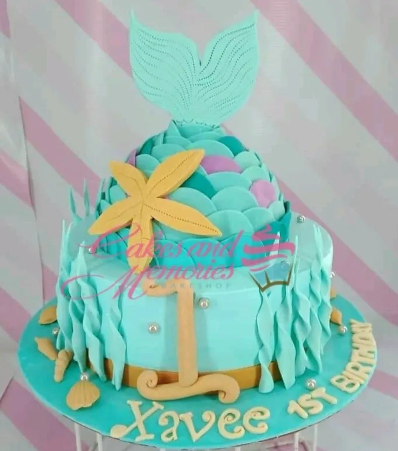 Mermaid themed 1-tier fondant cake with a large teal mermaid tail, yellow starfish, and sea-inspired gumpaste decorations. Mermaid themed 1-tier fondant cake with a large teal mermaid tail, yellow starfish, and sea-inspired gumpaste decorations.