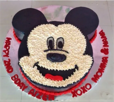 A black, white, and red 1-tier Mickey Mouse shaped cake, featuring white icing rosettes, black icing ears, and a red base border. A black, white, and red 1-tier Mickey Mouse shaped cake, featuring white icing rosettes, black icing ears, and a red base border.
