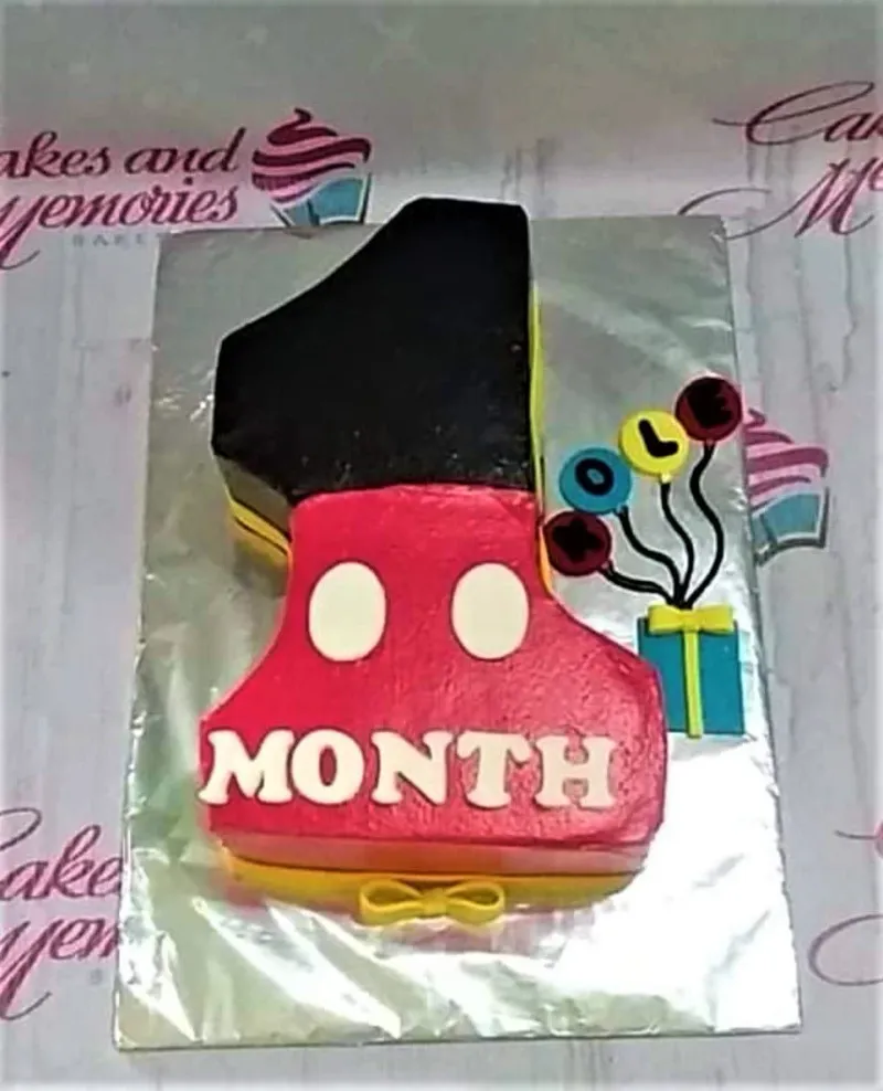 A red, black, yellow, and white rectangle cake shaped as number one, Mickey Mouse themed, with balloon and gift box printouts. A red, black, yellow, and white rectangle cake shaped as number one, Mickey Mouse themed, with balloon and gift box printouts.