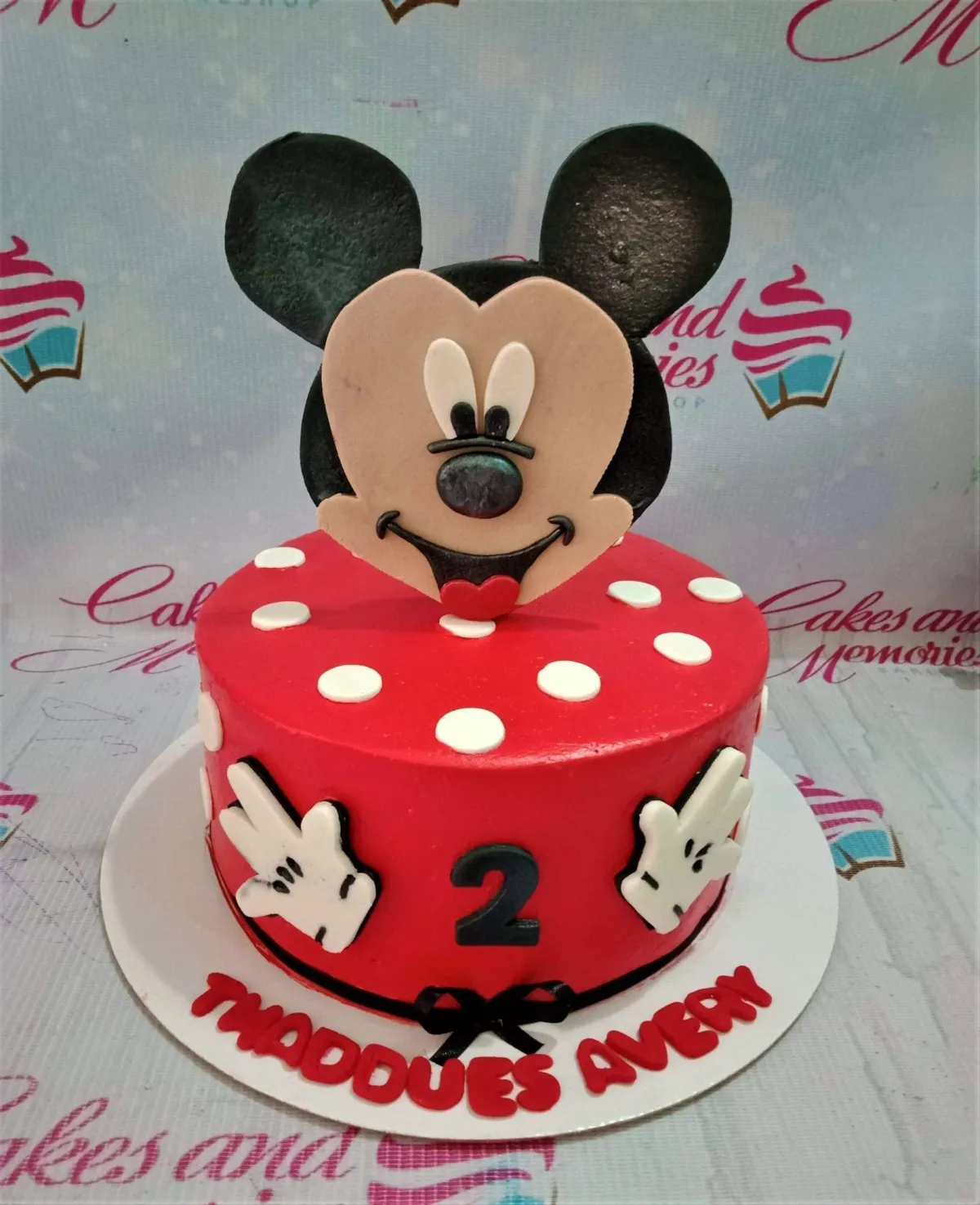 A red and white 1-tier cake themed around Mickey Mouse, featuring a fondant Mickey Mouse face topper, white polka dots, and Mickey gloves. A red and white 1-tier cake themed around Mickey Mouse, featuring a fondant Mickey Mouse face topper, white polka dots, and Mickey gloves.