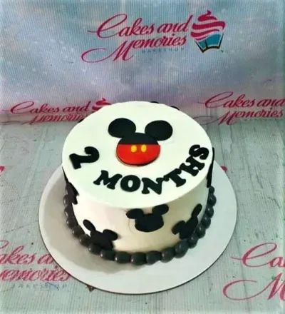 A white and black 1-tier Mickey Mouse cake, featuring a Mickey face topper, black silhouettes, and '2 MONTHS' text. A white and black 1-tier Mickey Mouse cake, featuring a Mickey face topper, black silhouettes, and '2 MONTHS' text.