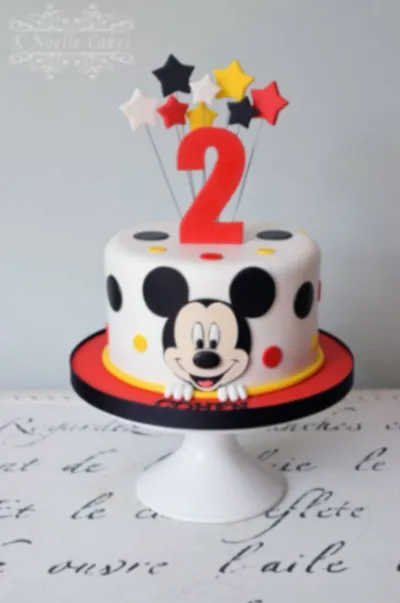 White fondant cake with a Mickey Mouse face panel, red number two topper, and colorful star accents White fondant cake with a Mickey Mouse face panel, red number two topper, and colorful star accents