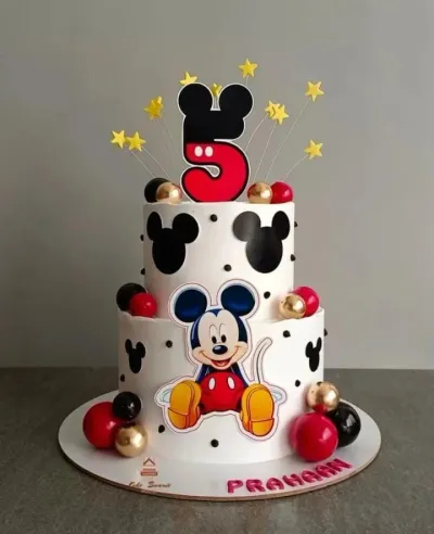 White 2-tier Mickey Mouse birthday cake with red, black, and gold spheres, Mickey silhouettes, and a large number 5 topper. White 2-tier Mickey Mouse birthday cake with red, black, and gold spheres, Mickey silhouettes, and a large number 5 topper.