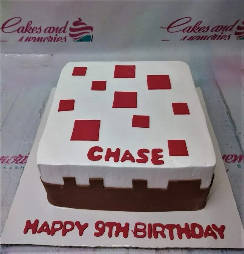 A white, brown, and red square cake themed around Minecraft, featuring a personalized name topper and red square accents. A white, brown, and red square cake themed around Minecraft, featuring a personalized name topper and red square accents.