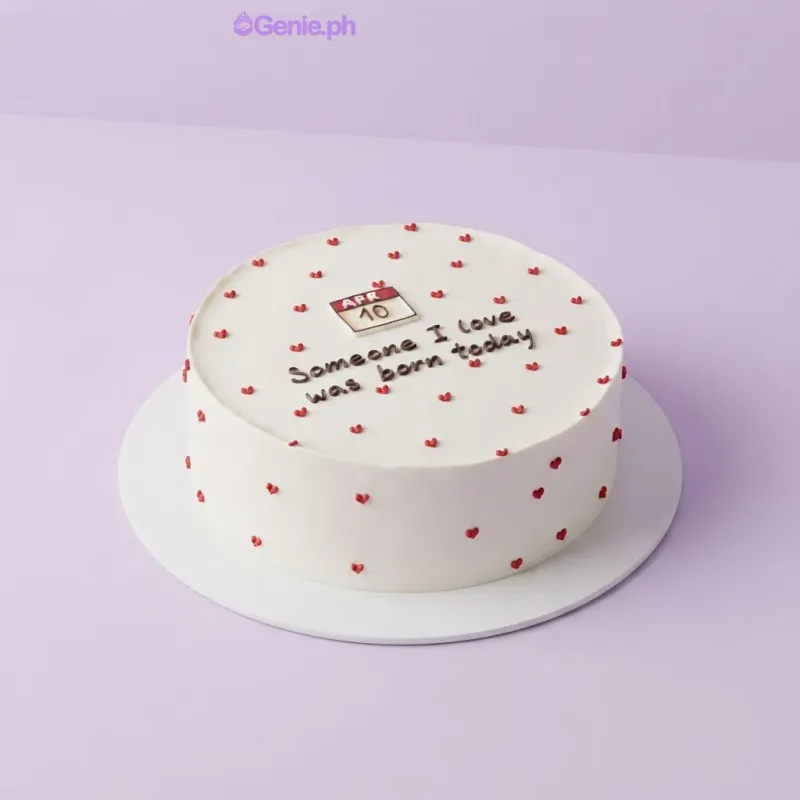 White 1-tier cake with smooth soft icing, a calendar printout topper, and small piped red heart accents White 1-tier cake with smooth soft icing, a calendar printout topper, and small piped red heart accents