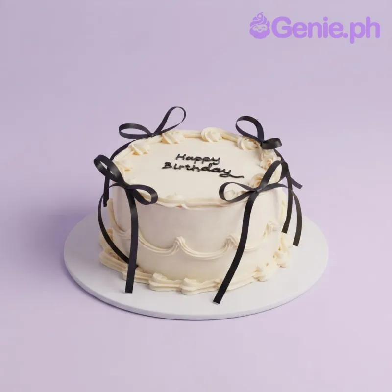 White 1-tier cake with soft icing, black ribbon bow accents, piped top border, and a tall black candle White 1-tier cake with soft icing, black ribbon bow accents, piped top border, and a tall black candle