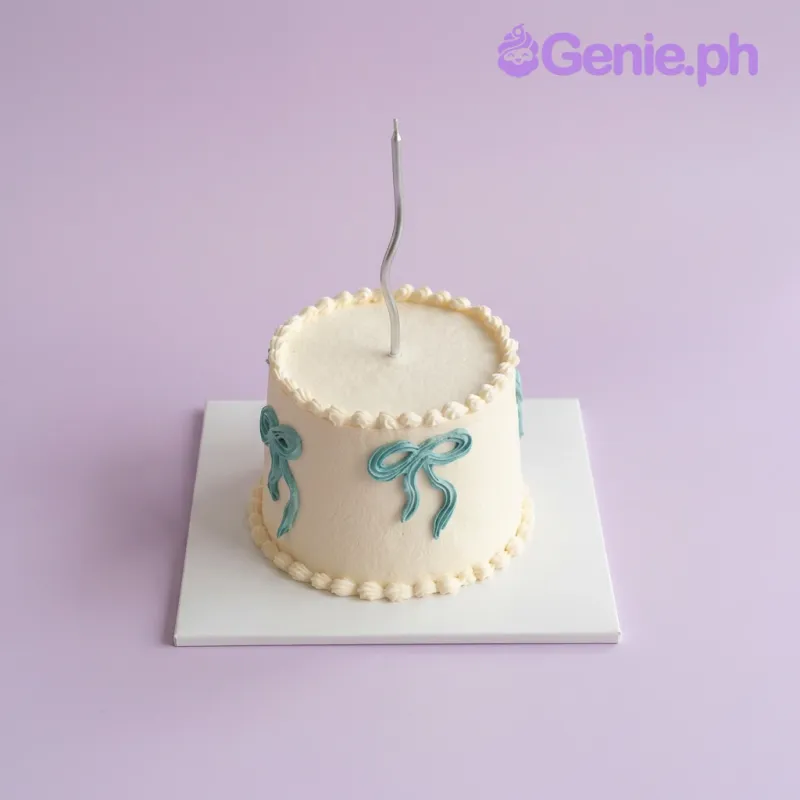 White 1-tier cake with piped blue bows and a single silver candle White 1-tier cake with piped blue bows and a single silver candle