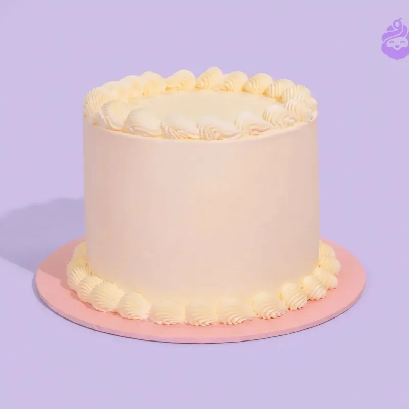 White single-tier cake with piped borders on a pink cake board White single-tier cake with piped borders on a pink cake board