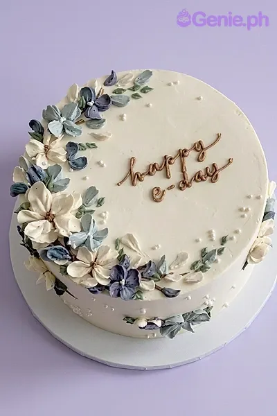 A white, blue, and ivory 1-Tier cake themed Minimalist Floral, featuring palette knife icing flowers and a brown piped message. A white, blue, and ivory 1-Tier cake themed Minimalist Floral, featuring palette knife icing flowers and a brown piped message.