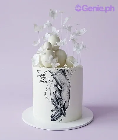 White minimalist cake featuring a hand-drawn sketch of two hands holding each other with white spheres and butterfly toppers. White minimalist cake featuring a hand-drawn sketch of two hands holding each other with white spheres and butterfly toppers.