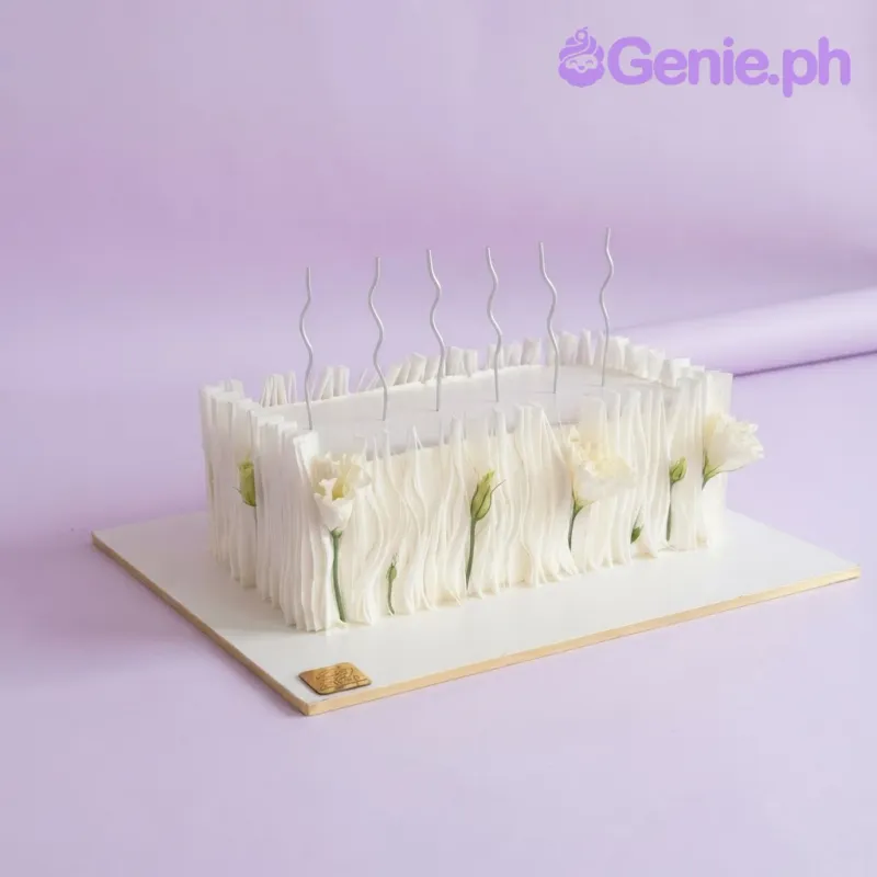 Minimalist white rectangle cake with soft icing, white eustoma flowers, and silver wavy candles Minimalist white rectangle cake with soft icing, white eustoma flowers, and silver wavy candles