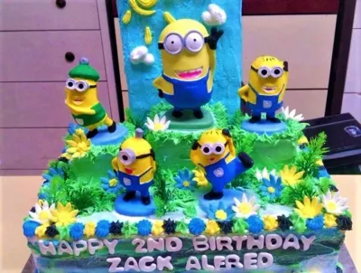 A blue and green 1 Tier cake themed around Minions, featuring five 3D Minion figures and grass-textured icing. A blue and green 1 Tier cake themed around Minions, featuring five 3D Minion figures and grass-textured icing.