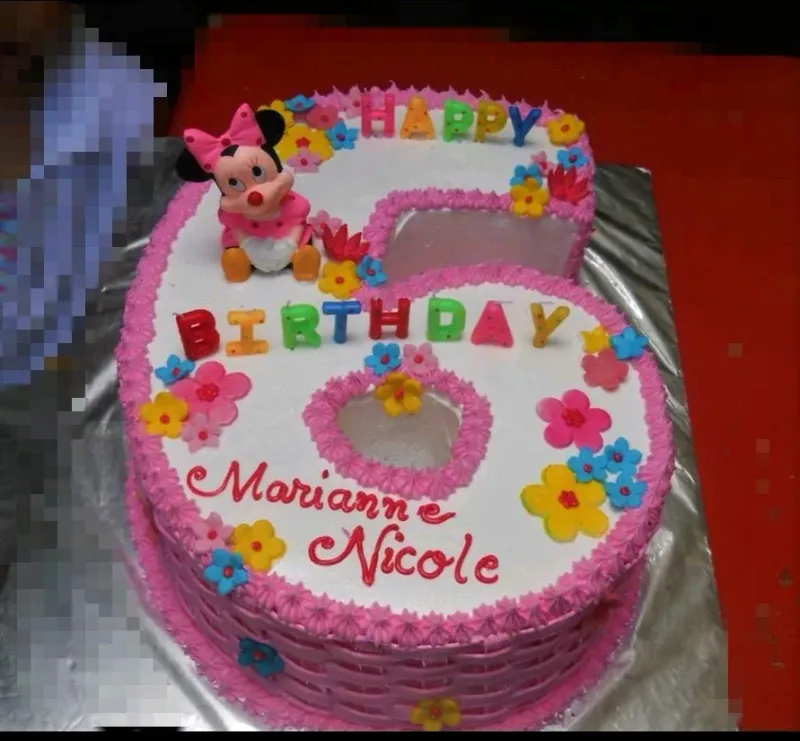 A pink and white Number 6 shaped Minnie Mouse cake with a Minnie Mouse figurine, 'HAPPY BIRTHDAY' candles, and edible flowers. A pink and white Number 6 shaped Minnie Mouse cake with a Minnie Mouse figurine, 'HAPPY BIRTHDAY' candles, and edible flowers.