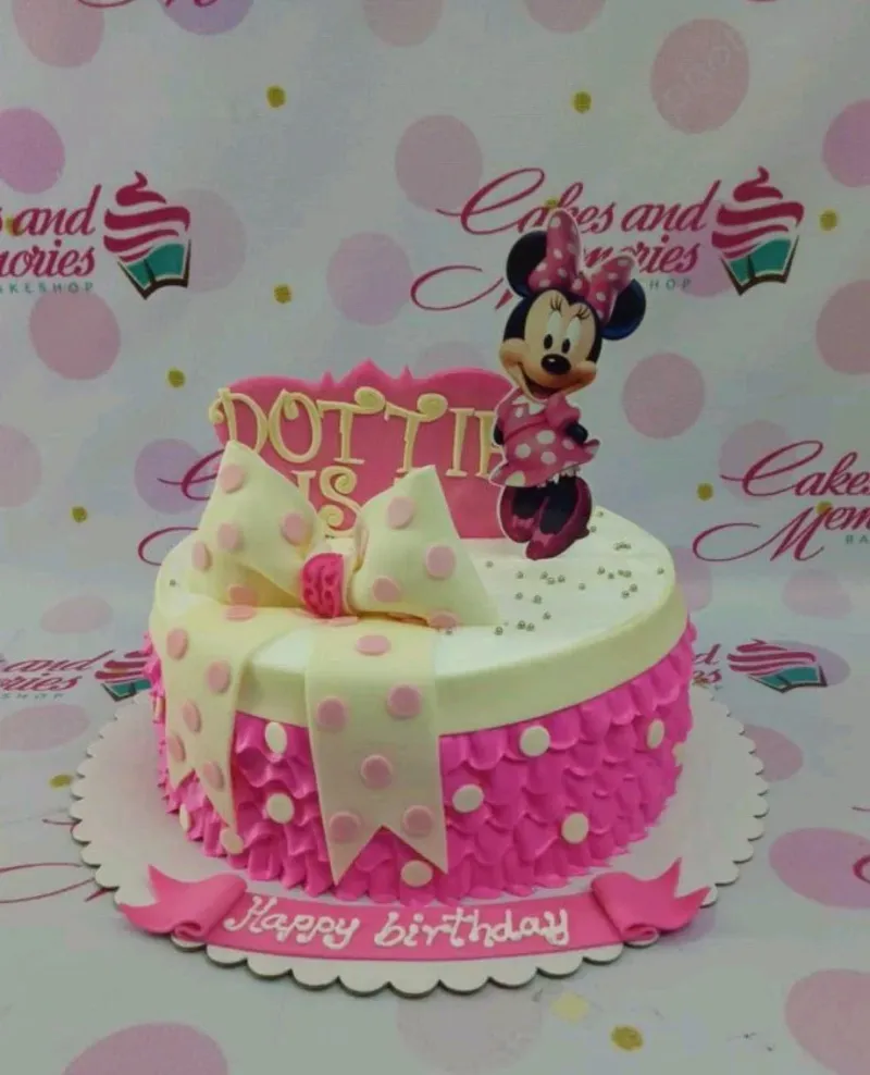 A pink and white 1-tier cake themed around Minnie Mouse, featuring a Minnie Mouse printout, a polka dot bow, and pink ruffles. A pink and white 1-tier cake themed around Minnie Mouse, featuring a Minnie Mouse printout, a polka dot bow, and pink ruffles.
