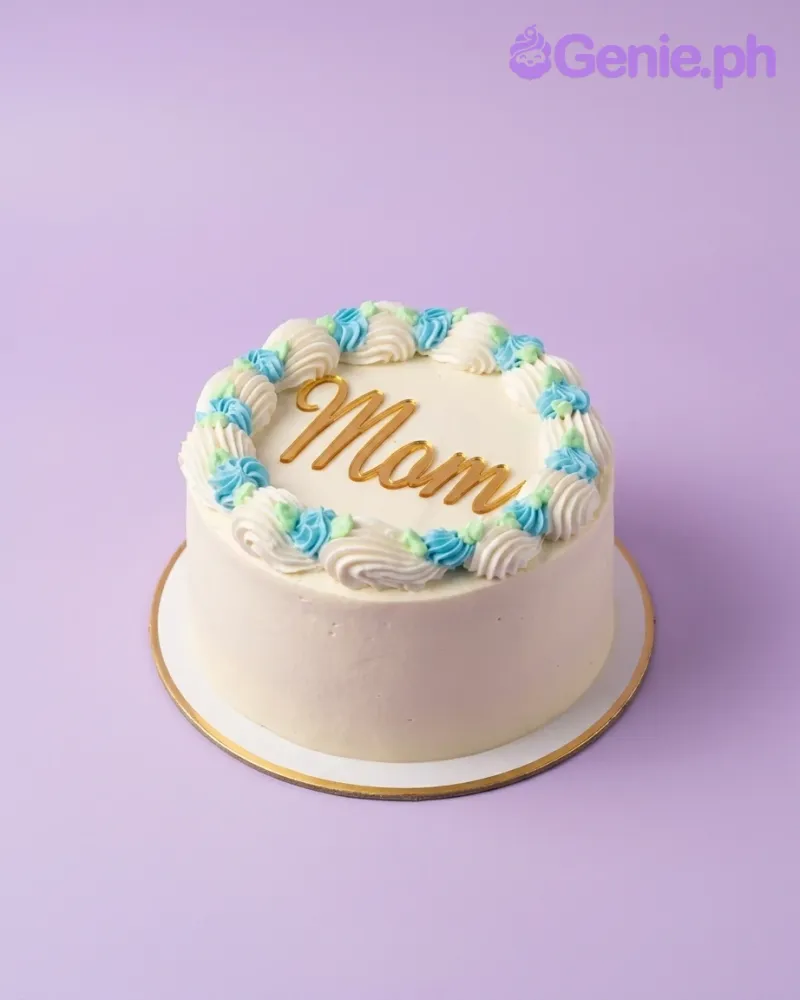 A white 1-tier cake themed around Mom Birthday, featuring a gold 'Mom' topper and blue, white, green rosettes with matching cupcakes. A white 1-tier cake themed around Mom Birthday, featuring a gold 'Mom' topper and blue, white, green rosettes with matching cupcakes.
