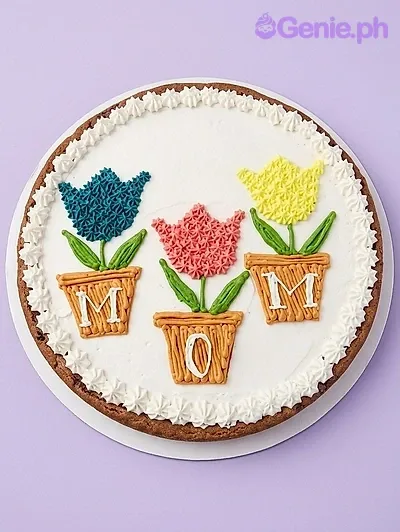 A white rectangular cookie cake themed MOM Tulip, with three piped icing tulip flower pots spelling MOM and an icing border. A white rectangular cookie cake themed MOM Tulip, with three piped icing tulip flower pots spelling MOM and an icing border.