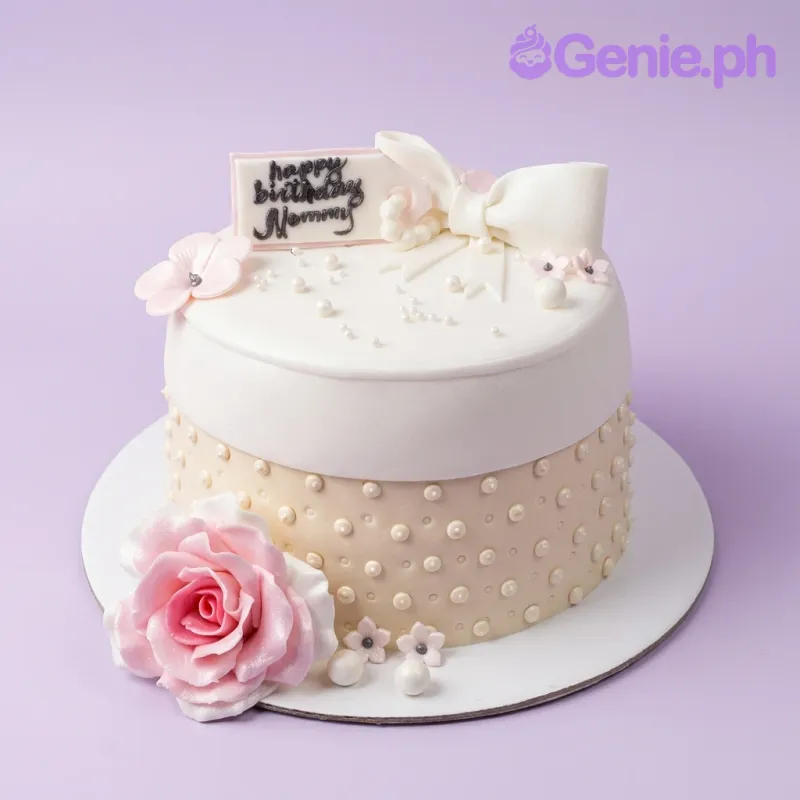 A white and cream 1 Tier Fondant Mommy Birthday cake, featuring a pink rose, white bow, and pearls. A white and cream 1 Tier Fondant Mommy Birthday cake, featuring a pink rose, white bow, and pearls.