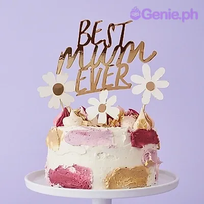 A white, pink, gold 1-tier Mother's Day cake, featuring a 'Best Mum Ever' topper, white daisies, and icing strokes. A white, pink, gold 1-tier Mother's Day cake, featuring a 'Best Mum Ever' topper, white daisies, and icing strokes.