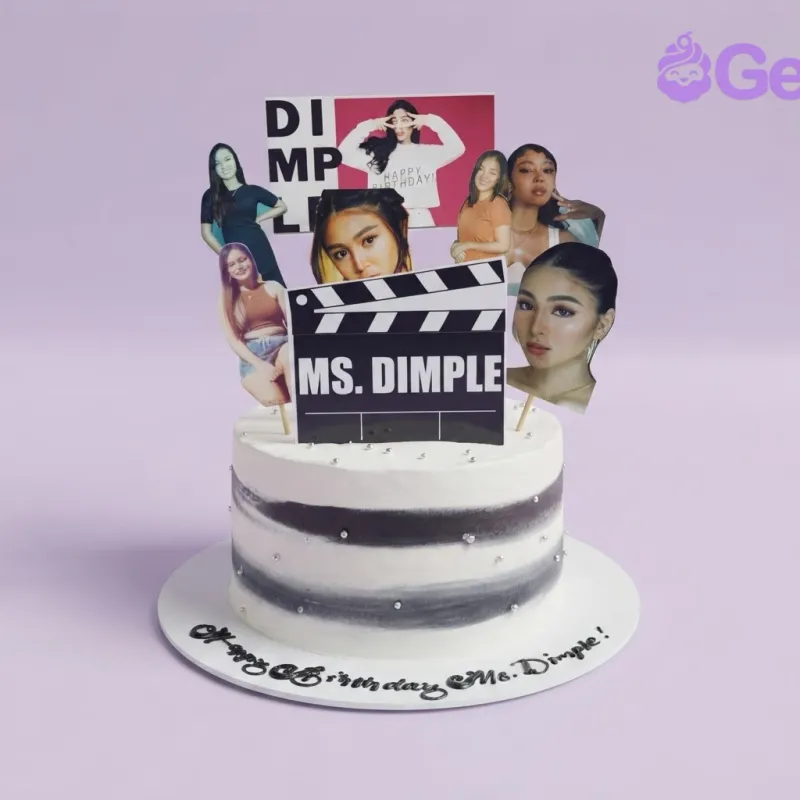 A white 1-tier Ms. Dimple cake, featuring a clapperboard, celebrity photos, black stripes, and silver dragees. A white 1-tier Ms. Dimple cake, featuring a clapperboard, celebrity photos, black stripes, and silver dragees.