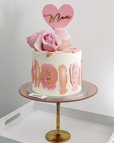 White 1-tier cake with pink and peach palette knife icing strokes, gold leaf accents, fresh pink roses, and a pink heart topper for Mum. White 1-tier cake with pink and peach palette knife icing strokes, gold leaf accents, fresh pink roses, and a pink heart topper for Mum.