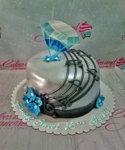 A silver fondant 1-tier cake, Music theme, with black musical notes, blue flowers, and a blue diamond printout. A silver fondant 1-tier cake, Music theme, with black musical notes, blue flowers, and a blue diamond printout.