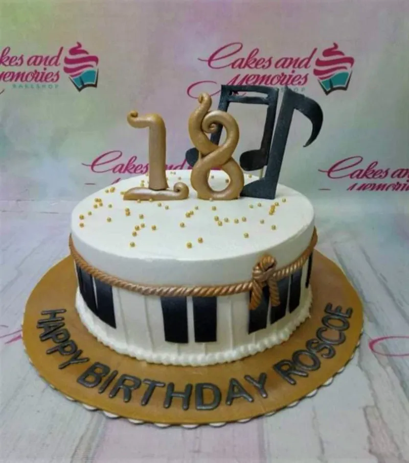White 1-tier music themed birthday cake with piano key side design, gold rope border, and gold 18 and music note toppers. White 1-tier music themed birthday cake with piano key side design, gold rope border, and gold 18 and music note toppers.