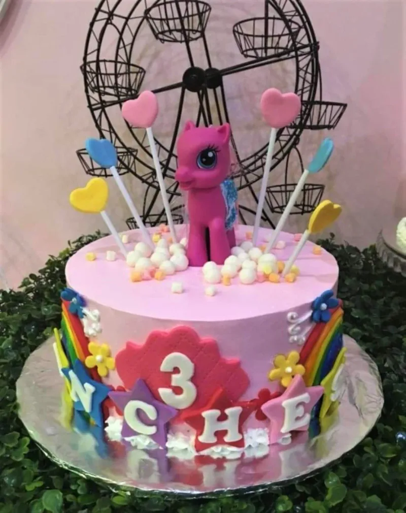 A pink 1-tier cake themed My Little Pony, featuring a Pinkie Pie figure and heart toppers, with rainbow side panels, stars, and flowers. A pink 1-tier cake themed My Little Pony, featuring a Pinkie Pie figure and heart toppers, with rainbow side panels, stars, and flowers.
