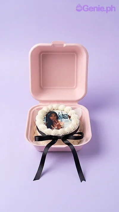 A white bento cake themed around Mystery Blind Box, featuring a printed photo of a person, white icing ruffles, and a black ribbon bow. A white bento cake themed around Mystery Blind Box, featuring a printed photo of a person, white icing ruffles, and a black ribbon bow.