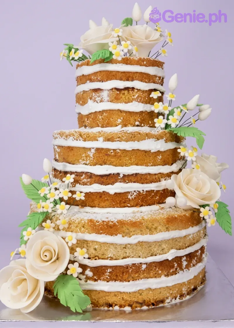 A white three-tier naked cake themed around Naked Floral, featuring white gumpaste roses, small yellow daisies, and green leaves. A white three-tier naked cake themed around Naked Floral, featuring white gumpaste roses, small yellow daisies, and green leaves.