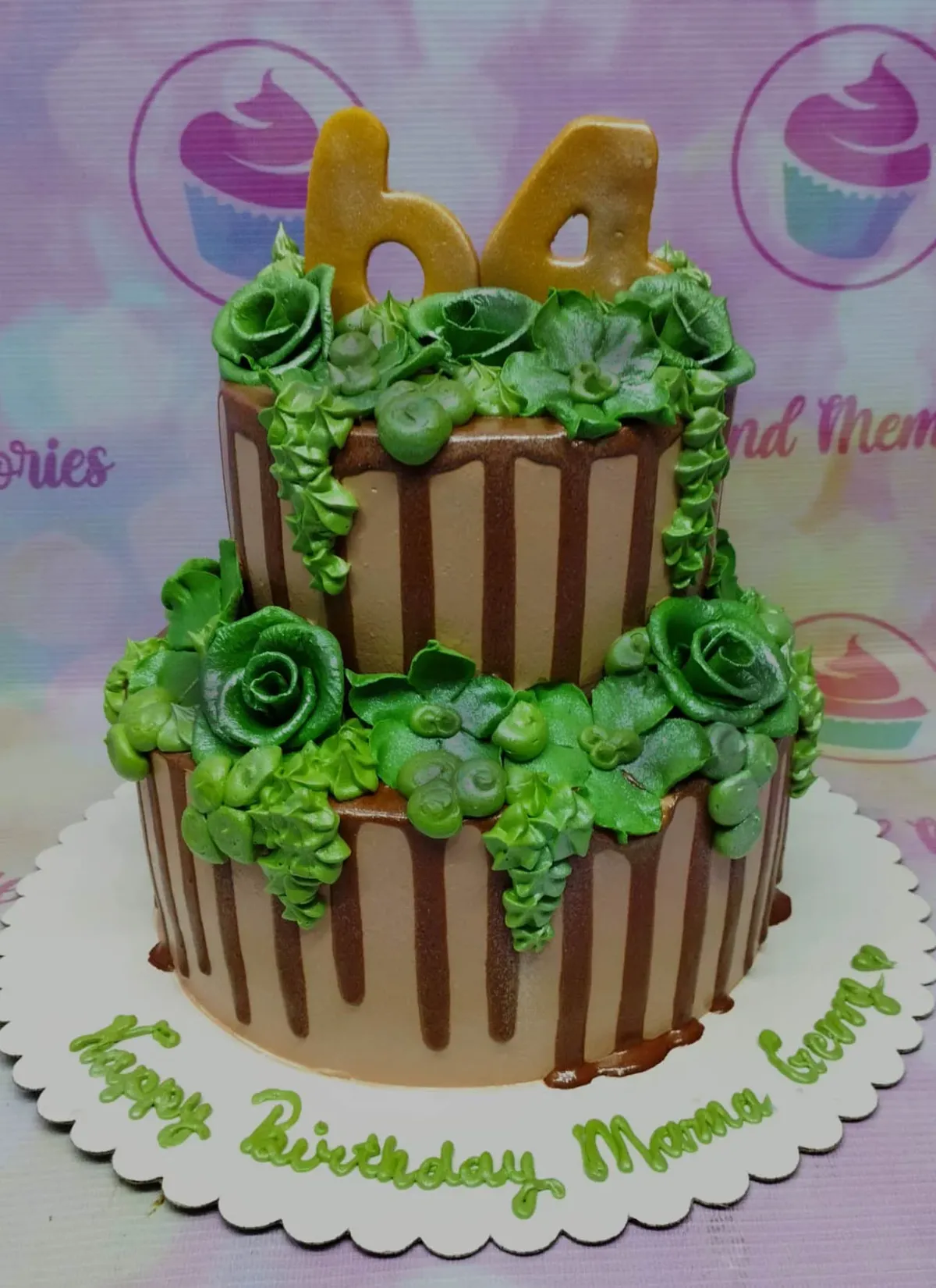 A brown and green two-tier nature cake, featuring a gold number 64 topper, green icing roses, leaves, and chocolate drips. A brown and green two-tier nature cake, featuring a gold number 64 topper, green icing roses, leaves, and chocolate drips.