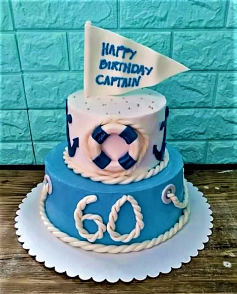 A white and light blue two-tier Nautical Captain cake, featuring flag, lifebuoy, fondant rope, and anchors. A white and light blue two-tier Nautical Captain cake, featuring flag, lifebuoy, fondant rope, and anchors.