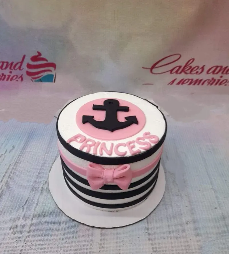 A white, black, and pink 1-tier Nautical Princess cake, with a pink anchor topper, 'PRINCESS' text, black stripes, and a pink bow. A white, black, and pink 1-tier Nautical Princess cake, with a pink anchor topper, 'PRINCESS' text, black stripes, and a pink bow.