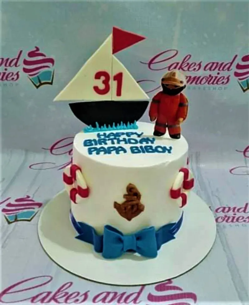A white 1 Tier Nautical Sailor cake with a fondant sailor, a sailboat with '31', lifebuoys, and an anchor. A white 1 Tier Nautical Sailor cake with a fondant sailor, a sailboat with '31', lifebuoys, and an anchor.