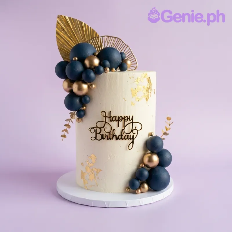 A white 1-tier cake themed Navy and Gold, featuring gold palm leaf fans, black 'Happy Birthday' text, navy blue and gold spheres, and gold leaf accents. A white 1-tier cake themed Navy and Gold, featuring gold palm leaf fans, black 'Happy Birthday' text, navy blue and gold spheres, and gold leaf accents.