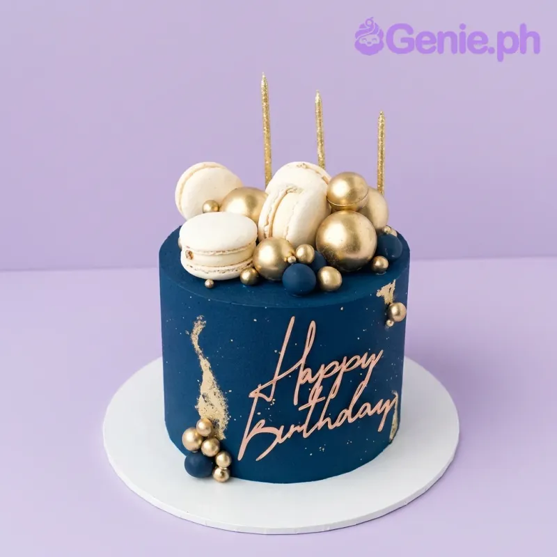 A navy blue 1-Tier birthday cake with gold spheres, white macarons, and a rose gold 'Happy Birthday' topper. A navy blue 1-Tier birthday cake with gold spheres, white macarons, and a rose gold 'Happy Birthday' topper.