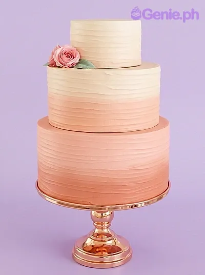 Elegant three-tier ombre pink cake with horizontal textured icing and a single pink rose accent on the top tier. Elegant three-tier ombre pink cake with horizontal textured icing and a single pink rose accent on the top tier.