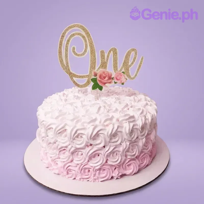 A pink and white ombre 1-tier cake for a first birthday, featuring a gold glitter 'One' topper with pink roses and piped rosettes. A pink and white ombre 1-tier cake for a first birthday, featuring a gold glitter 'One' topper with pink roses and piped rosettes.