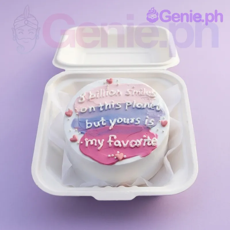 A white bento cake with pink, purple, and blue palette knife icing strokes, a white piped message, and pink heart decorations. A white bento cake with pink, purple, and blue palette knife icing strokes, a white piped message, and pink heart decorations.