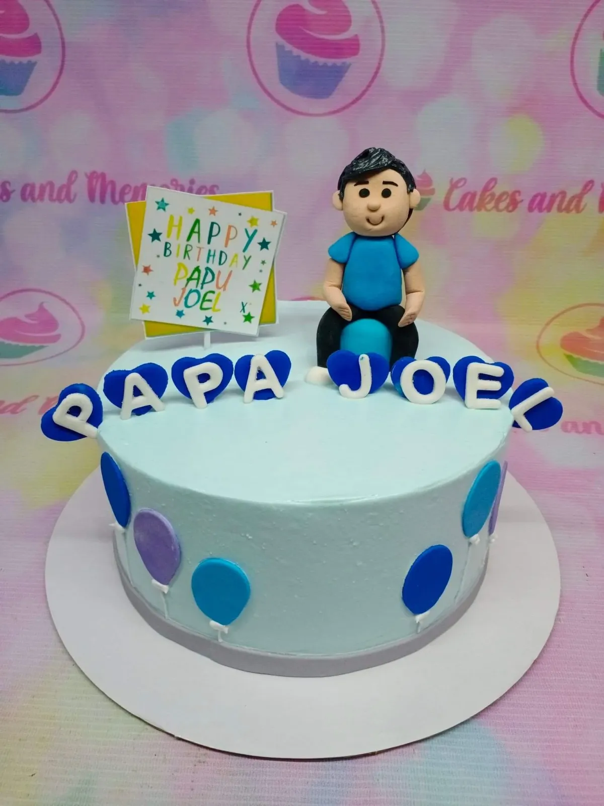 Light blue birthday cake for Papa Joel featuring a 3D fondant man figure, balloon decorations, and a Happy Birthday sign. Light blue birthday cake for Papa Joel featuring a 3D fondant man figure, balloon decorations, and a Happy Birthday sign.