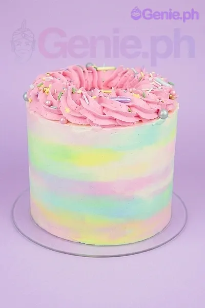 A single-tier cake with pastel rainbow watercolor icing, topped with pink icing rosettes, colorful sprinkles, and silver pearls. A single-tier cake with pastel rainbow watercolor icing, topped with pink icing rosettes, colorful sprinkles, and silver pearls.