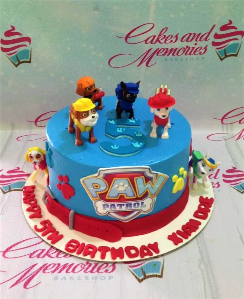 A blue 1 Tier Paw Patrol cake, featuring character toys, a logo, a blue number 5, a red fondant belt, and paw prints. A blue 1 Tier Paw Patrol cake, featuring character toys, a logo, a blue number 5, a red fondant belt, and paw prints.